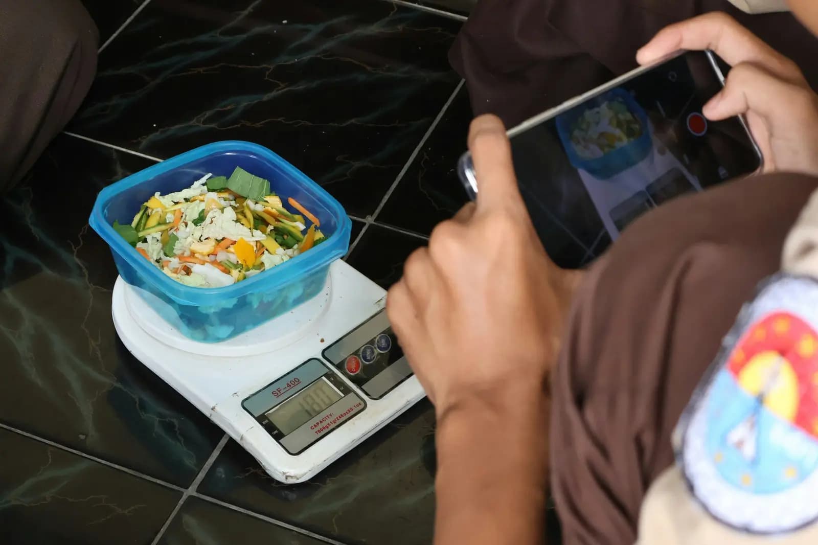 Food weighed on a digital kitchen scale while a phone records the weight