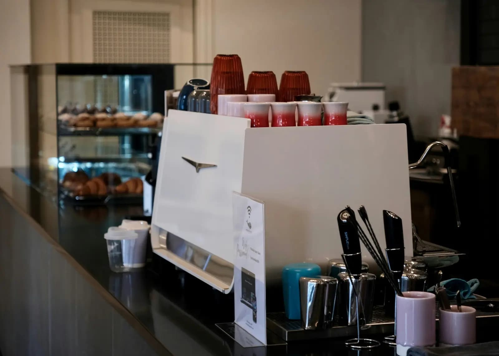 Espresso machine and cups on a cafe counter with pastries behind